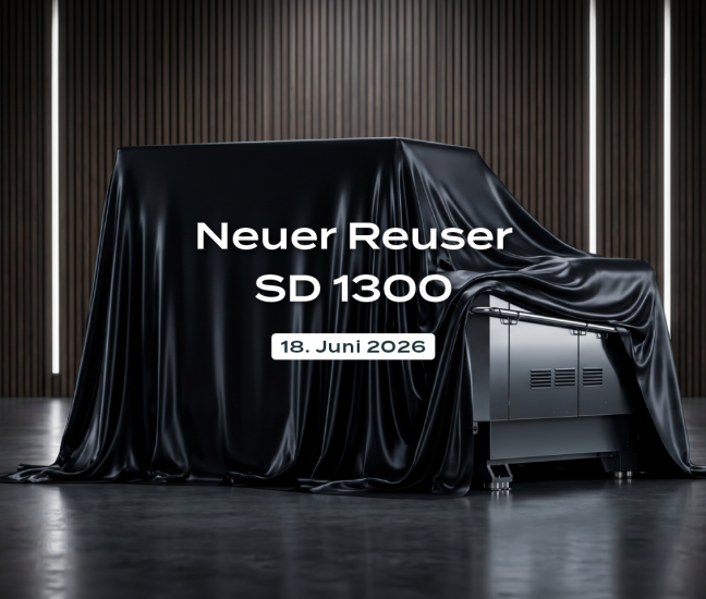 Industrieller Einwellen-Zerkleinerer Robust Reuser SD 1300, geheimnisvoll mit einem schwarzen Tuch verhüllt in einem modernen Showroom. Das Bild enthält das Robust Reuser Logo und den Text: Neuer Reuser SD 1300, 18. Juni 2026.